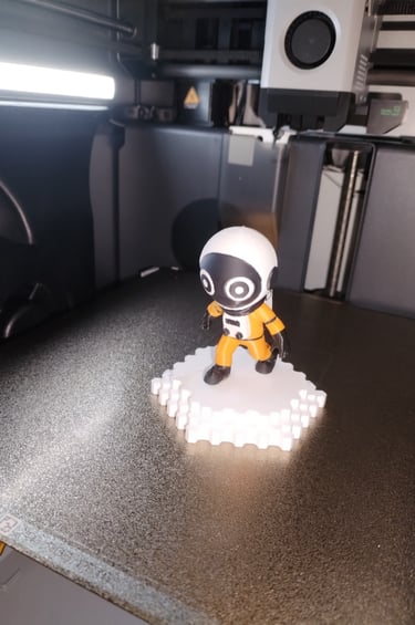 Figurine d’astronaute imprimée en 3D par OptiPrint3D, en combinaison orange sur socle blanc.