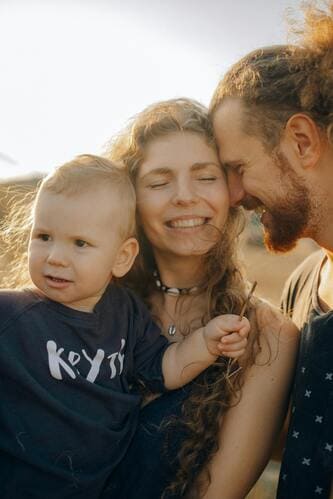 Una familia feliz con una madre, un padre y un niño pequeño sonrientes al aire libre al atardecer