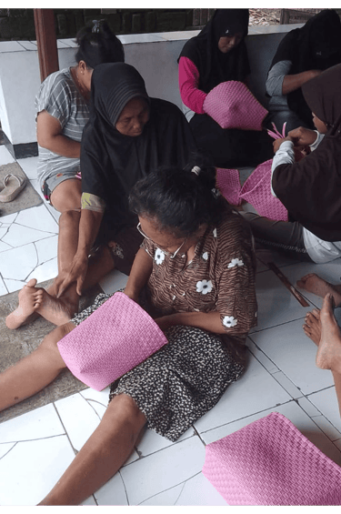 Artisan weaving a pink jali jali plastic woven bag by hand at Craftvitas Indonesia.