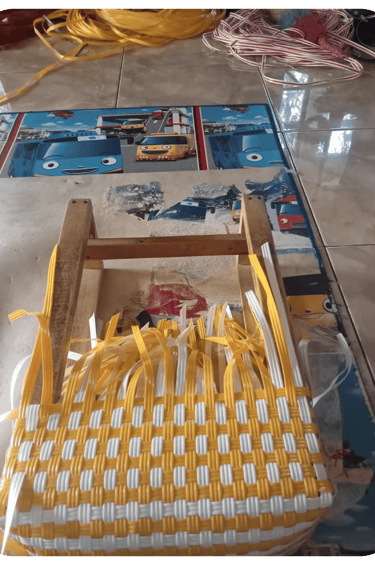 Shaping the base of a yellow and white handmade woven bag using recycled plastic weaving strips at Craftvitas Indonesia.