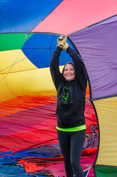 A woman holds open a colorful rainbow hot air balloon envelope during inflation.