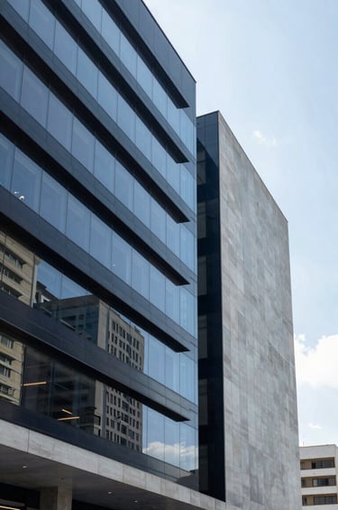 A professional shot of a modern architectural building interior in a South American / Brazilian city, featuring clean lines and glass facades. The lighting is bright and airy, conveying expertise and forward-thinking. The color palette is dominated by dark navy blue and soft blue-grey tones.
