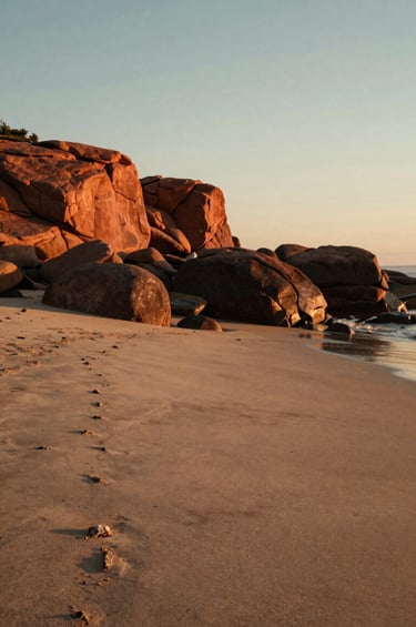 A cinematic landscape shot of a North American / US coastal setting at sunset, bathed in warm, sun-drenched light. The scene is peaceful and authentic, with textures of soft sand and deep terracotta rocks. A professional lifestyle photography style that feels approachable and rich with storytelling potential.
