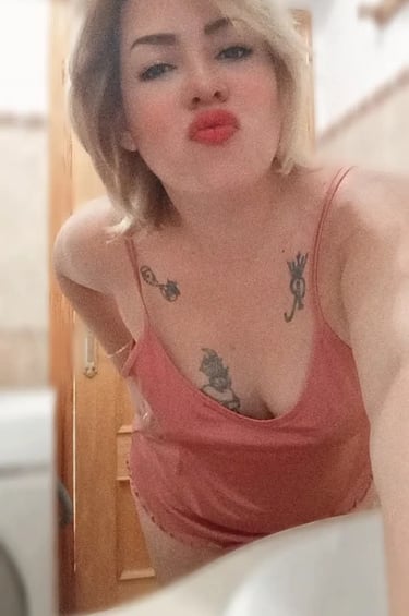 Selfie de Nikol con pijama rosa, labios sensuales y tatuajes visibles en el pecho
