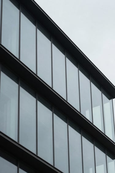 An abstract architectural photograph of a modern building with clean lines and glass textures, reflecting a pale gray sky, sharp focus, minimalist composition, professional and elegant aesthetic.