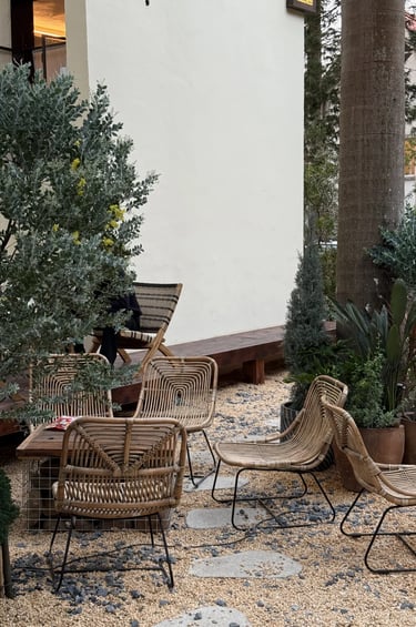 Woven outdoor chairs in a natural garden corner with gravel, plants and soft textures, creating a re