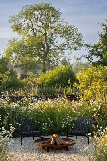Naturalistic garden with mature trees, soft planting, outdoor chairs and a fire bowl, showing how ti