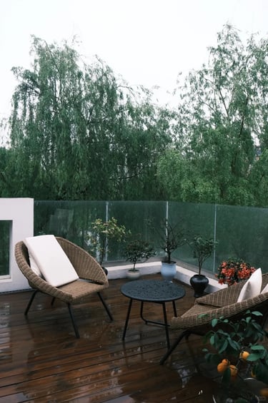 Small outdoor seating area with wicker chairs, a round table, wooden decking and greenery in a moder