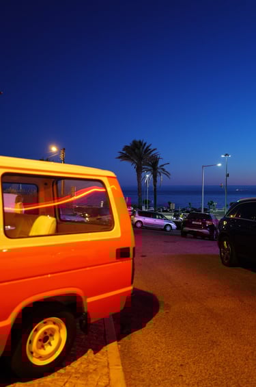 Orange van parked by the seaside at dusk with palm trees in Cascais, Portugal, By ACAT Phot