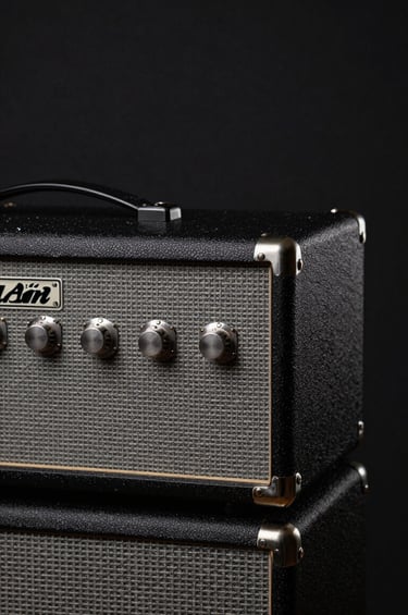 Close-up photography of a weathered guitar amplifier in a dark studio setting. The lighting is low-key, highlighting textures of medium gray and deep black. Minimalist and professional style, reflecting an authentic artistic vibe in a Western European setting.