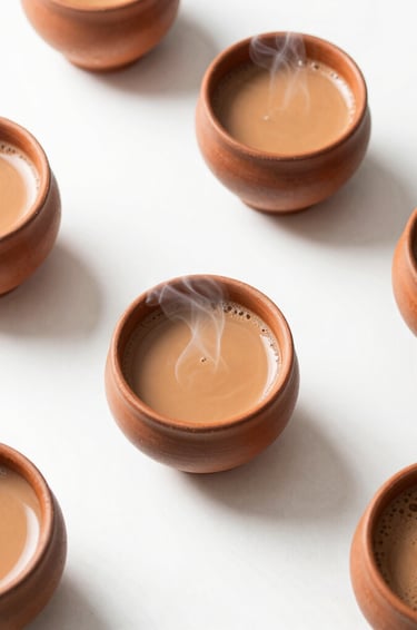 Overhead flat-lay of steaming clay cups of chai on a clean, bright white table under soft natural daylight.