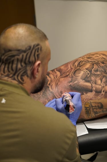Professional tattoo artist with head ink working on a large back piece using a rotary machine.