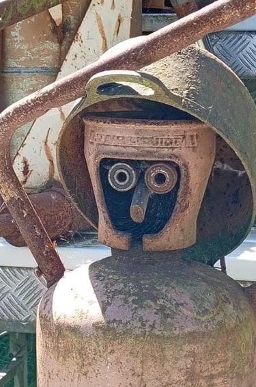 Rusty vintage gas cylinder modified into a scrap metal sculpture of a human face with a helmet.