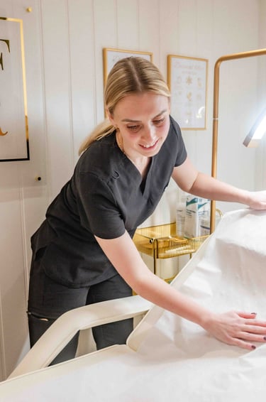 Aesthetician in black scrubs preparing a medical treatment bed at House of Harper Aesthetics clinic.