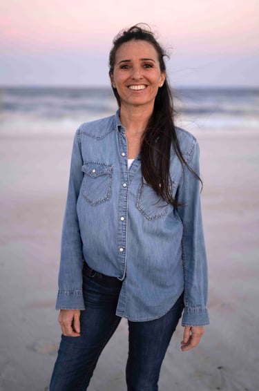 Michael Alexa Pitts standing on a flat beach at dusk smiling with a dusty blue ocean and soft pink sky behind 