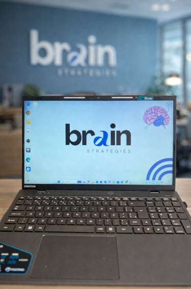 Positivo laptop displaying the Brain Strategies logo on a desk in a modern corporate office setting.