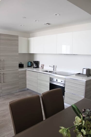 Modern minimalist kitchen with light wood grain cabinets, white upper units, and built-in appliances.