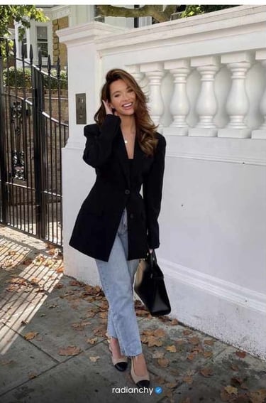 a woman in a black jacket and jeans standing in front of a fence