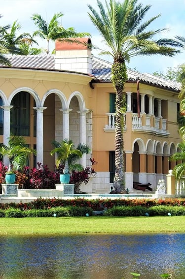 Luxury waterfront Mediterranean villa with white arches and tall palm trees reflected in the lake.
