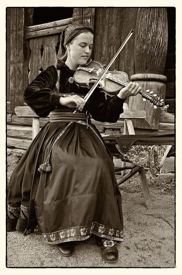 A black and white photo of a woman in traditional dress playing a hardanger violin