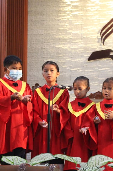 Little kids wearing red church robe singing on a stage