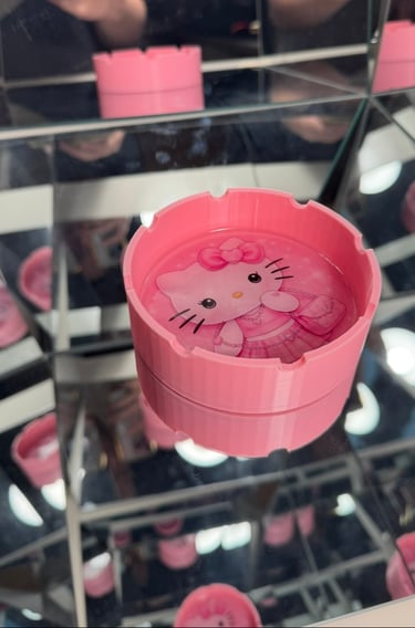 Pink Hello Kitty ashtray with character design on a mirrored surface reflecting multiple angles.