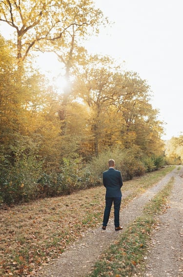 Le marié attend la mariée dans un chemin forestier aux couleurs d'automne, pour leur first look.