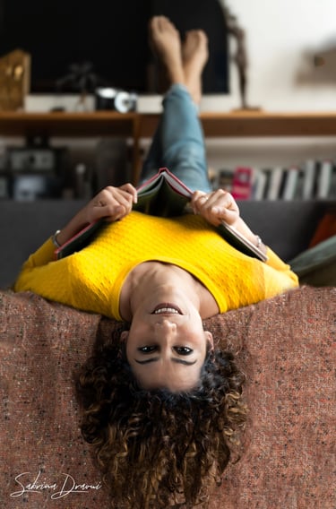 a corporate woman upside down laying on a couch with a book 
