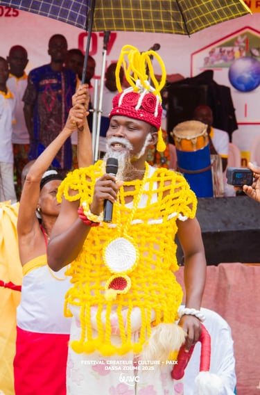 A performer in traditional Beninese attire and yellow woven regalia speaks at a Dassa-Zoumé cultural festival.