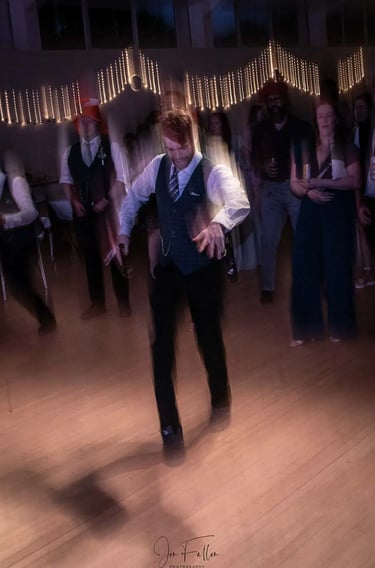 A groom dancing on a wooden dance floor during a wedding reception with motion blur and fairy lights.