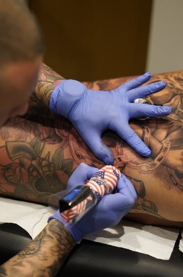 Professional tattoo artist wearing blue gloves using an American flag machine on a detailed back piece.