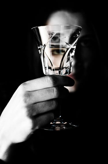 Hand holding a crystal wine glass with a silhouette of a woman in the dark background.