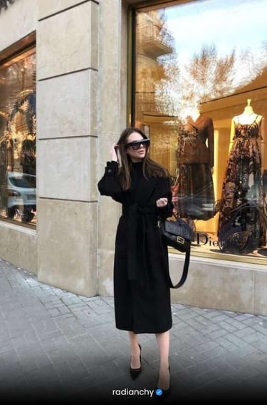 a woman in a black dress and sunglasses is standing in front of a store window
