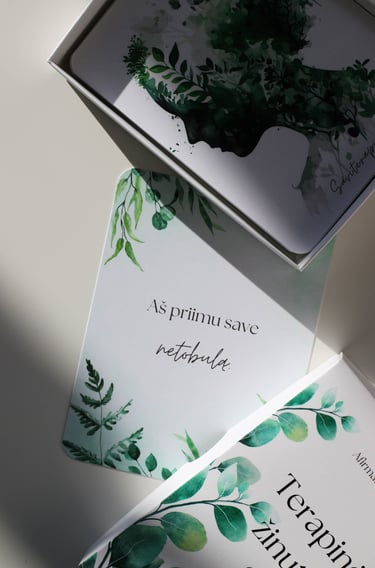 Afirmacijų kortelės su žaliais lapais; matoma kortelė su tekstu „Aš priimu save netobulą"