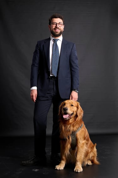 A man in a navy blue suit and tie posing with his golden retriever dog against a dark studio background.