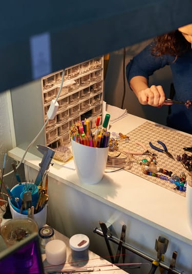 Creador de joyería usando alicates en un escritorio con cuentas de vidrio y materiales de artesanía 