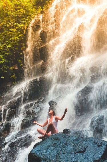 a woman embracing nature while sitting on a rock in front of a waterfall
