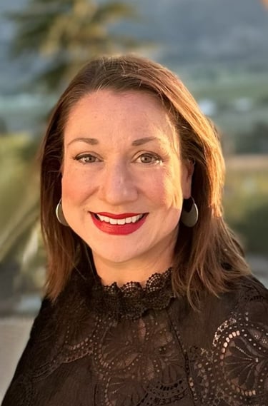 Professional headshot of a smiling woman with red lipstick, brown hair, and a black lace top.