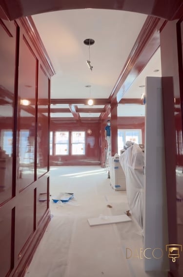 Professional painter applying high-gloss red lacquer finish to custom home library wood paneling.