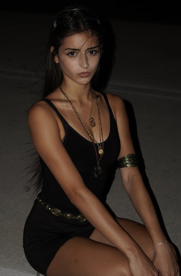 A young woman wearing a black mini dress and gold statement jewelry for a night aesthetic look.