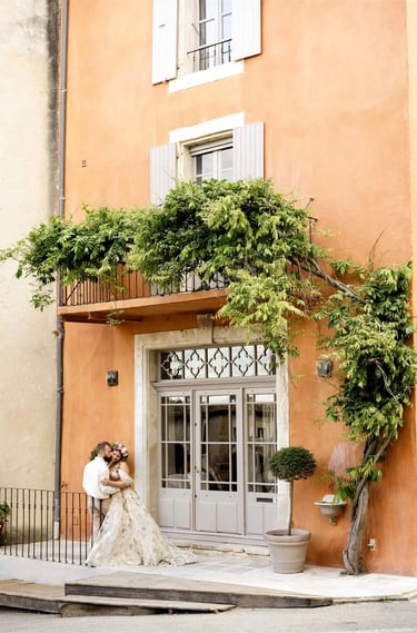 Wide shot of couple in front of ochre building with climbing vine — kiss on the cheek, fine art