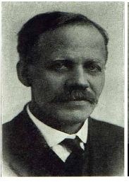 a headshot of a stern looking man with a mustache