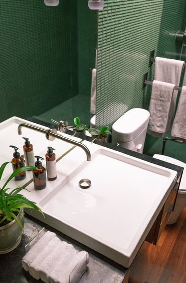 une salle de bain avec plan vasque design, carrelage mosaïque vert, toilettes et sèche serviettes