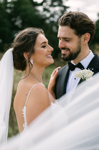 couple portrait of the bride and groom looking at each other smiling while the veil blows in wind
