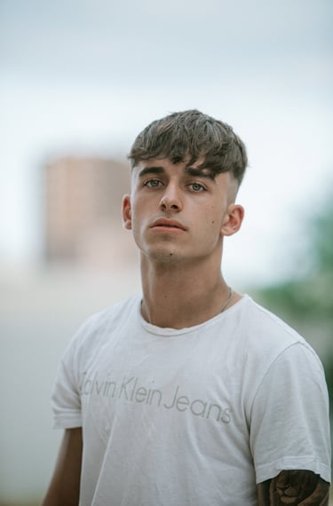 Primer plano del modelo con camiseta blanca y gafas de sol Hawkers, con Seat León rojo de fondo