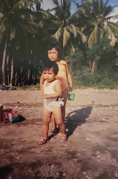 My sister and I on the beach, tropical foliage in the background.