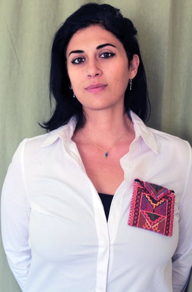 A woman wearing a white button-down shirt featuring a colorful embroidered textile pocket.