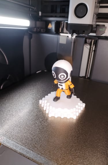 Figurine d’astronaute imprimée en 3D par OptiPrint3D, en combinaison orange sur socle blanc.