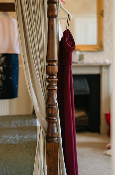 Red bridesmaid dress hanging from an antique four-poster bed at The Mill House Hotel