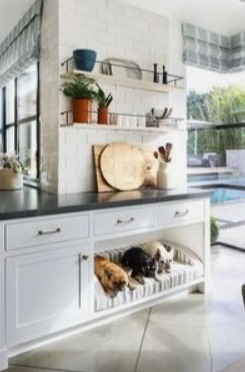 Three dogs resting in a built-in kitchen island pet bed under a white marble countertop.